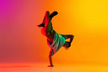 Gordijnen Portret van een stijlvolle jongeman, breakdance-dansertraining in vrijetijdskleding geïsoleerd over een roze gele achtergrond met kleurovergang in de danszaal in neonlicht. © master1305