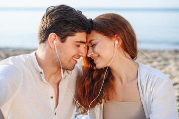 Close up happy young couple two family man woman in white clothes hug sitting sand listen to music...
