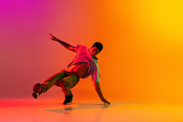 Caucasian man, break dancing dancer ptacticing in casual clothes isolated over gradient pink yellow background at dance hall in neon light.