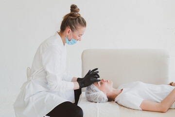 Beautician masseur doing facial massage to young woman