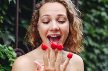 Close up young excited happy caucasian woman in pink dress put girl put raspberries on fingers eat...