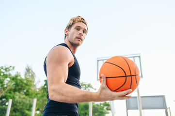 Side bottom view serious muscular young sporty sportsman man 20s wearing black sports clothes training holding in hand ball play at basketball game playground court. Outdoor courtyard sport concept