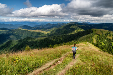 Fototapeta na wymiar Female hiker with backpack and trekking poles on hiking trail