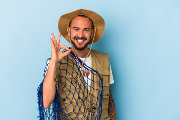Young caucasian fisherman with tattoos holding net isolated on blue background  cheerful and...