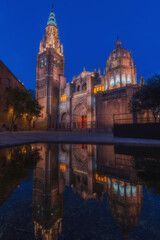 Cityscape in old city night light change; Toledo old town cathedral square with reflection in the water of the fountain - artificial lake, world heritage site, Spain. Vertical view