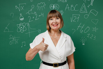 Happy teacher mature elderly lady woman 55 years old wear shirt showing thumb up like gesture isolated on green wall chalk blackboard background studio. Education school September 1 concept