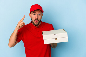 Young caucasian delivery man with tattoos holding pizzas isolated on blue background  having an idea, inspiration concept.