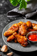 Homemade baked or fried chicken wings in barbecue sauce in a gray ceramic plate on a black cooking table close-up. Dark background
