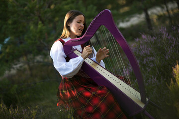 Beautiful young woman playing celtic harp and singing song in woodland