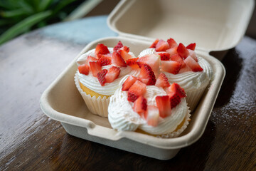 Homemade buttercream cupcakes with fresh strawberries in a take away container on wooden table.
