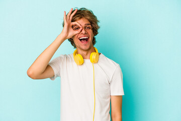 Young caucasian man listening to music isolated on blue background  excited keeping ok gesture on...