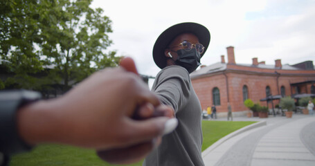 Follow me shot of african man in hat and safety mask leading woman to street in European city