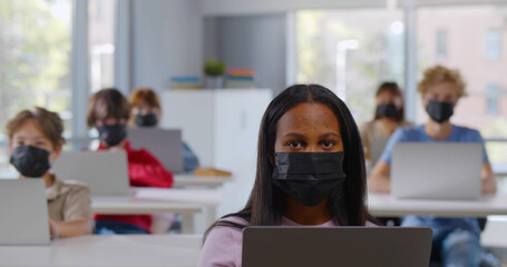 African schoolgirl put on medical mask using laptop during lesson looking at camera