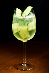 Cocktail with alcohol, cucumber slices, herbs and ice cubes on a wooden table with blurred background