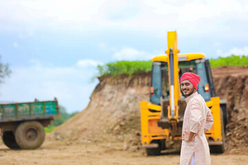 Indian farmer standing with his new earth mover machinery.