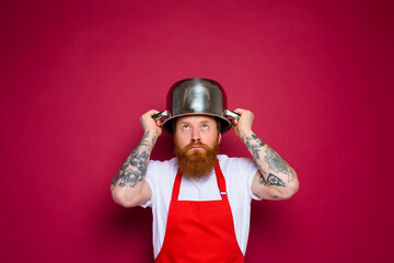 Fototapeta na wymiar worried chef with beard and red apron plays with pot