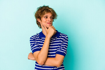 Young caucasian man with make up isolated on blue background  looking sideways with doubtful and skeptical expression.