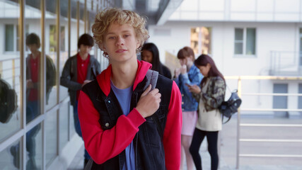 Teen boy looking at camera with classmates talking on background.