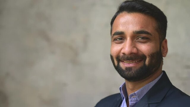 Smiling middle-age Indian high skilled leader ceo manager in formal suit looks at the camera, confident ambitious bearded arabic businessman stands in office with arms folded on the grey background