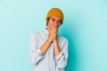 Young caucasian man with make up isolated on blue background  laughing about something, covering mouth with hands.