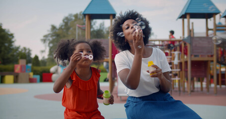 Afro-american mother and daughter play soap bubbles at playground. - Powered by Adobe