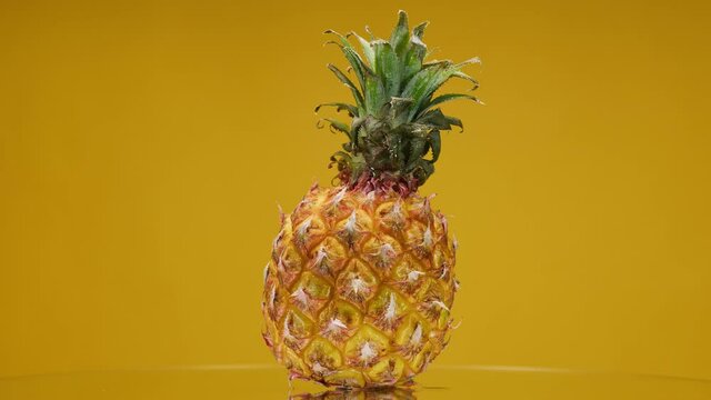 Close-up of rotating ripe pineapple on yellow background, making a cocktail of fruits or berries, drinking cold lemonade, shooting of fresh sliced fruits.