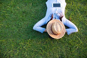 Woman lay down sleep on green grass meadow garden summer sunshine day happy time outside. Hipster Freelance work on laptop use hat cover face sleep on grass field. Relax Woman lying down green garden © aFotostock