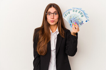 Young caucasian business woman holding banknotes isolated on white background shrugs shoulders and open eyes confused.