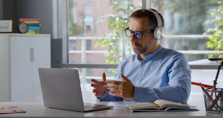 Mature teacher in headphones having online class on laptop