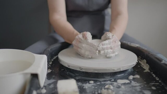 Elderly woman master works on a potter's wheel and makes a mug of ceramics in her workshop in slow motion