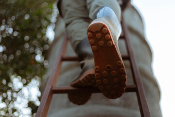 Gardening concept a male farmer wearing big boots climbing on a wooden ladder to a cement water tank