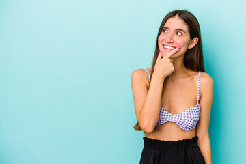 Naklejka premium Young caucasian woman wearing bikini isolated on blue background looking sideways with doubtful and skeptical expression.
