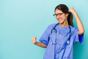 Young caucasian nurse isolated on blue background raising fist after a victory, winner concept.