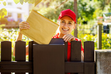 smiling postman mail carrier inserting envelope into mailbox - obrazy, fototapety, plakaty