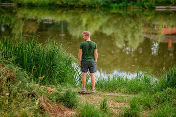 Fototapeta na wymiar Rear view a young man stands on the shore of a beautiful summer lake