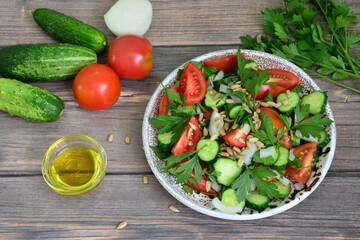 vegetable salad with cherry tomatoes, cucumber, onion, parsley, olive oil and sunflower seeds on brown tiramisu plate on dark wooden background