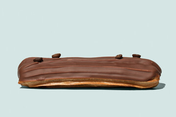 Chocolate eclair with coffee beans on light blue background isolated