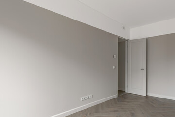 Fototapeta na wymiar Simple Modern Beige-Grey Wall with grey light switch and grey socket in the Empty Room with open door and oak wood floor. Interior Design Element of contemporary interior design at modern house