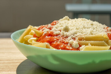 Popular recipe for children of macaroni with tomato and grated cheese on a blue plate