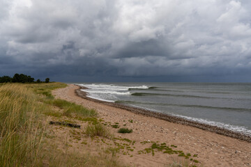 neat waves breaking on a sandy beach with marsh grass and sand dunes and a dark ominous sky overhead