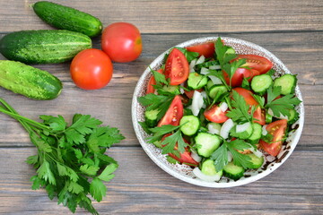 vegetable salad with cherry tomatoes, cucumber, onion, parsley, olive oil on brown tiramisu plate on dark wooden background
