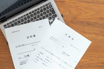 Obraz premium ノートブックPCに置かれた病気療養のための休職届と診断書（左）