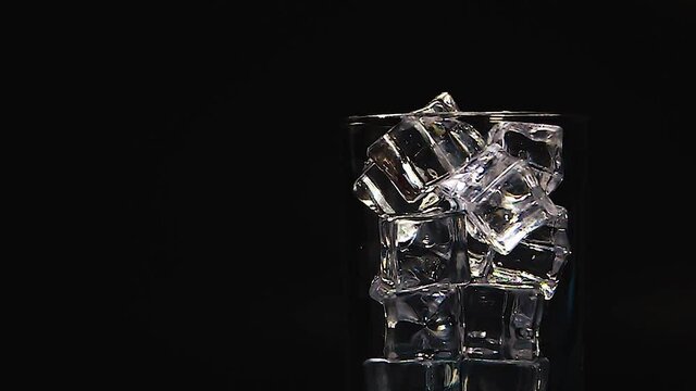Clear soft drink poured into a glass with square ice cubes, clear bubbles spread, with a black background, leaving a place to put letters