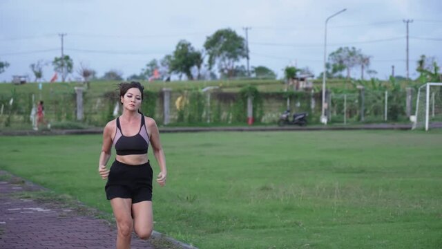 A beautiful mixed-race girl runs a marathon against the background of a green stadium on a sunny day. The athlete is struggling to train in running in a large open stadium. Woman runs in slow motion