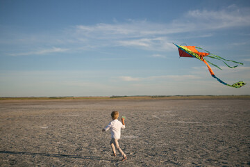 a boy runs with a kite at sunset on the shore of the salt lake of the sea