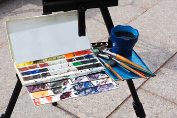 Artist painting on the street. Street artist, plein air. Brushes and paints on the easel