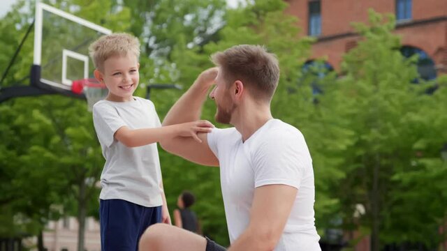 Father showing muscles to little son exercising together outdoors