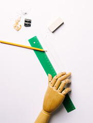 Artificial wooden hand holding green ruler and graffiti pen on Bright white paper background. Creative designer or architectural project concept. Flat lay, top view.