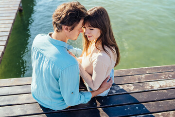 Couple of two, man and woman, sitting together on pier of wooden bridge in the sea or lake and...