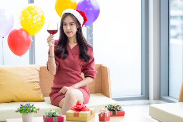 An Asian young girl celebrating the Christmas and new year 2022. Woman in red dress sipping red wine with gift boxes and balloons